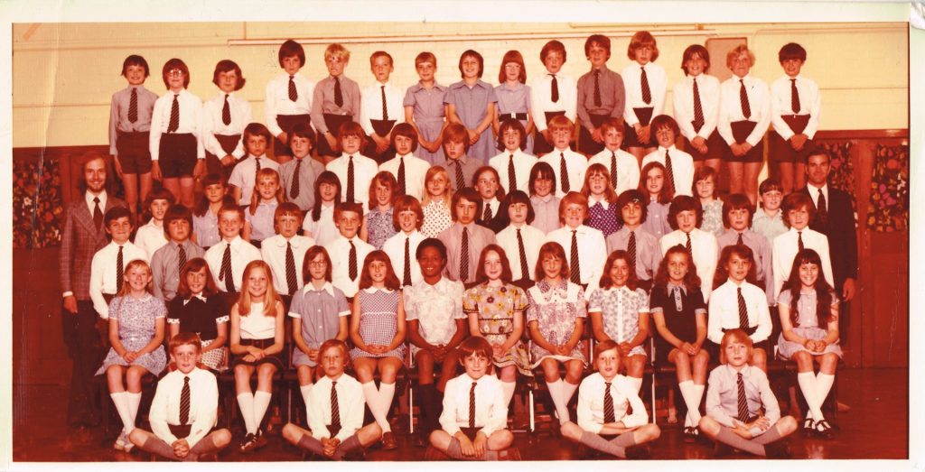 Primary school children lined up for their final year photo. The front are sitting cross-legged then they tier up to the back row. 