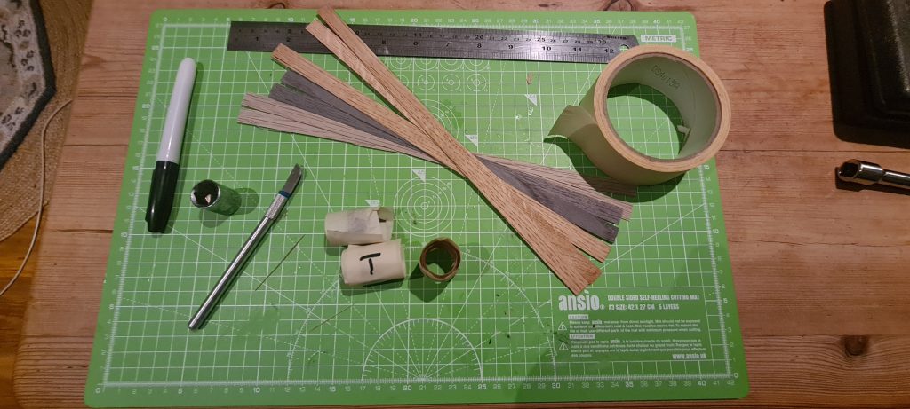 Things you need to make a bentwood ring. A ruler, a scalpal, some wood veneer, a socket from a garage set and some masking tape. These are all sitting on a cutting board.