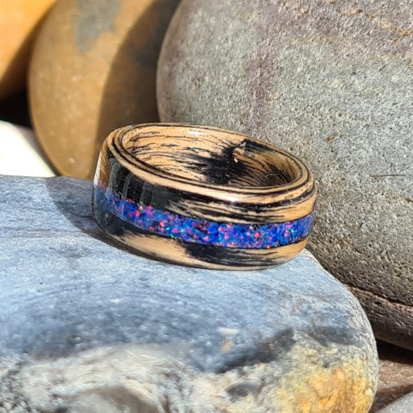 Ebonised oak ring with blue opal inlay resting on beach stones.